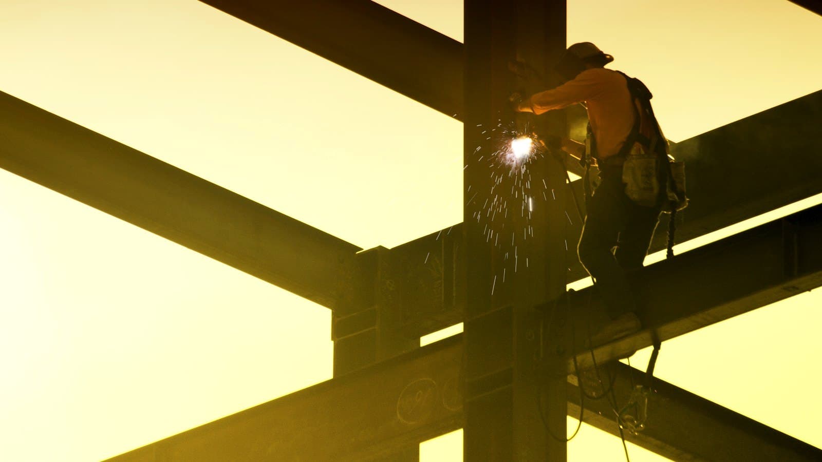 Welder cutting a steel column and beams against a golden sky