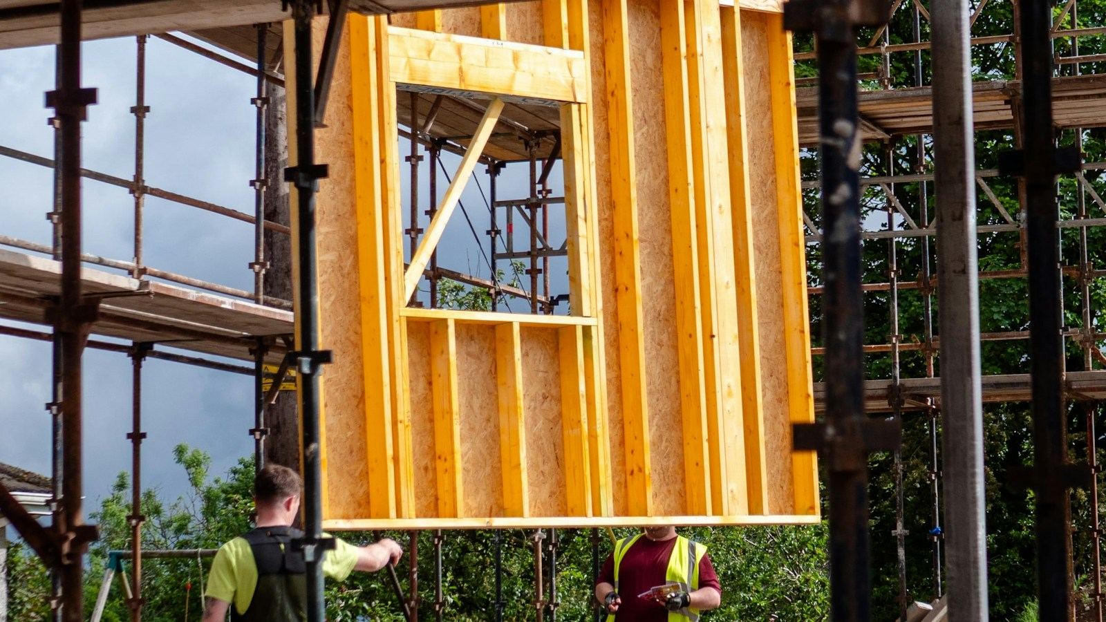 Timber frame wall panel with a window opening being craned into place between scaffolding